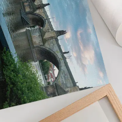 Spauda ant drobės tiltas per upę su istorine architektūra ir ramybės pojūčiu