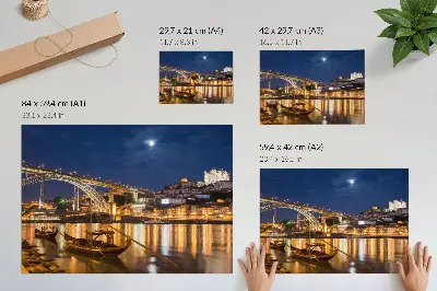 Plakatas tiltas naktį su šviečiančiu miestu ir valtimis vandenyje